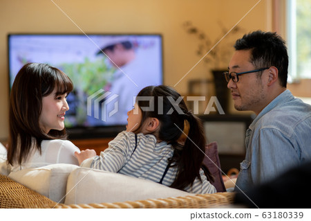 Image of three parents and children (father, mother, daughter) watching TV on the sofa Image of three parents and children (father, mother, daughter) watching TV on the sofa 63180339