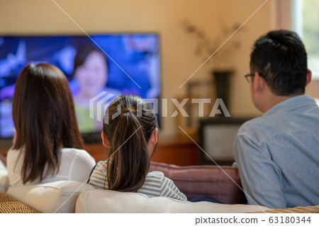 Image of three parents and children (father, mother, daughter) watching TV on the sofa Image of three parents and children (father, mother, daughter) watching TV on the sofa 63180344