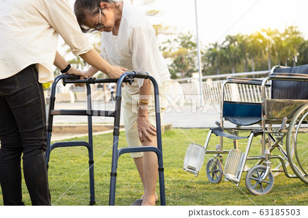 Senior asian female patient hand to touch her knee,have joint hurt,bone problem,painful in the knees while walk use walker during rehabilitation,elderly woman suffer from osteoporosis,gout,rickets 63185503