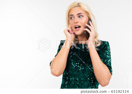 charming woman with blond hair in a green shiny dress is talking on the phone on a white background 63192314