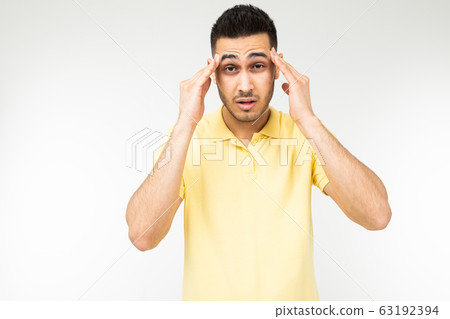 brunette man feels a severe headache and holds his head in his hands on a white studio background 63192394