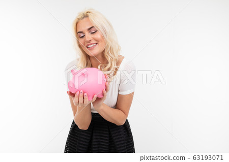 charming blonde woman in a white t-shirt holds a piggy bank on a white background with copy space charming blonde woman in a white t-shirt holds a piggy bank on a white background with copy space 63193071