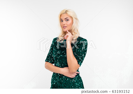 girl in elegant green shiny dress makes a pensive look on a white studio background girl in elegant green shiny dress makes a pensive look on a white studio background 63193152