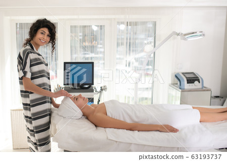 Dark-haired beautiful cosmetologist in striped shirt working with a client 63193737
