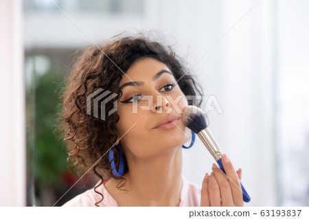 Dark-haired woman applying powder on her face 63193837