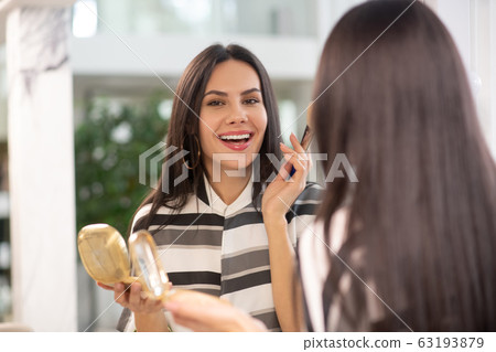 Dark-haired woman doing her make up and smiling Dark-haired woman doing her make up and smiling 63193879