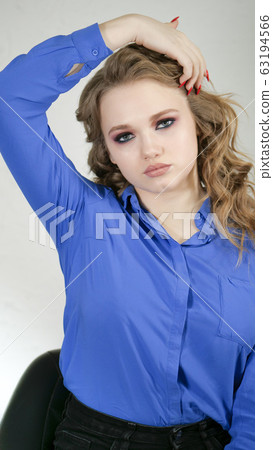 Girl is blonde with curly hair in a bright blue shirt. Hand touches the hair. Girl is blonde with curly hair in a bright blue shirt. Hand touches the hair. 63194566