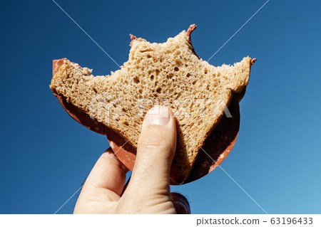 bitten vegan salami sandwich in the hand. 63196433