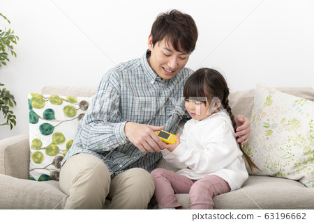 Parent and child (father and daughter) family image sitting on the sofa in the living room and watching a kids mobile phone Parent and child (father and daughter) family image sitting on the sofa in the living room and watching a kids mobile phone 63196662
