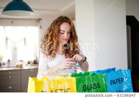 Young woman indoors at home separating glass, paper, and plastic waste. 63196847
