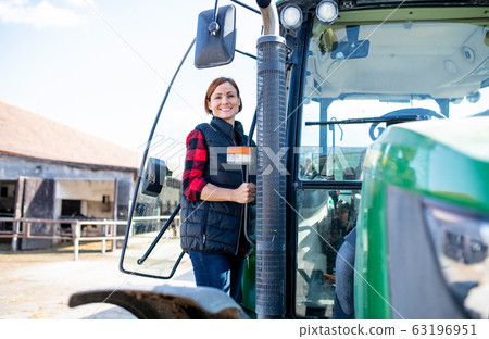 Woman worker standing by tractor on diary farm, agriculture industry. Woman worker standing by tractor on diary farm, agriculture industry. 63196951