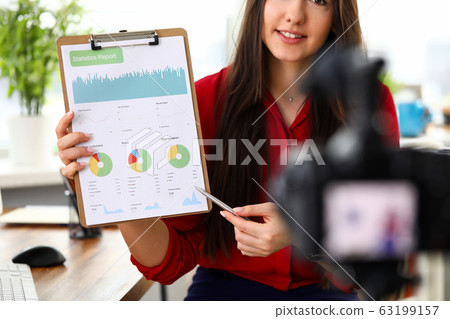 Young woman sitting in office opposite camera and presenting statistics and analytics report. Young woman sitting in office opposite camera and presenting statistics and analytics report. 63199157