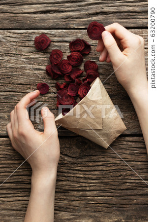 Home-made beet chips. Snacks are wrapped in a paper bag. Hand holds food bag. Handmade healthy vegetables chips 63200790