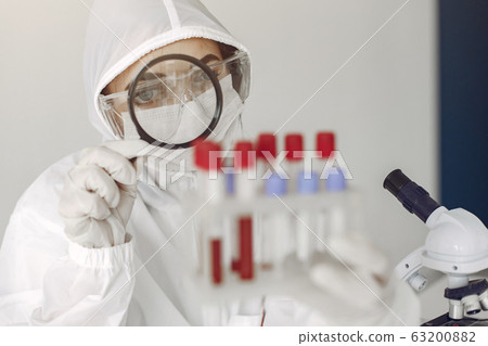 Scientist in coverall clothing is examining coronavirus sample in a laboratory 63200882