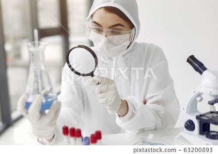 A laboratory scientist is examining blue solution in a bottle 63200893