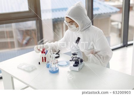 Laboratory worker in coverall suit is adjusting microscope 63200903