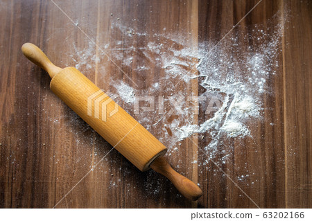 Flour is scattered on a brown wooden background-table and a rolling pin lies. View from above 63202166