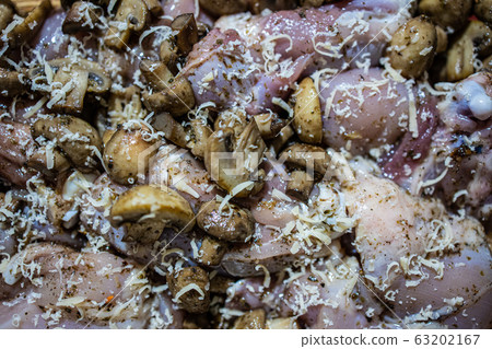 Raw chicken thigh sprinkled with champignons and grated cheese before baking. Close-up Raw chicken thigh sprinkled with champignons and grated cheese before baking. Close-up 63202167