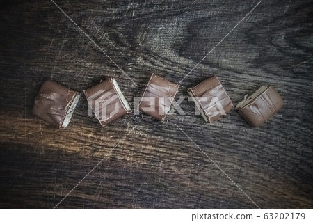 A chocolate bar cut into pieces lies on a dark wooden background. Copy space, flat lay. 63202179