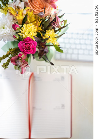 A stylish bouquet with fresh spring flowers is on the desktop near the keyboard and handwritten 63202256