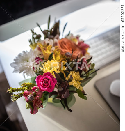 A stylish bouquet with fresh spring flowers is on the desktop near the computer, keyboard and mouse 63202271