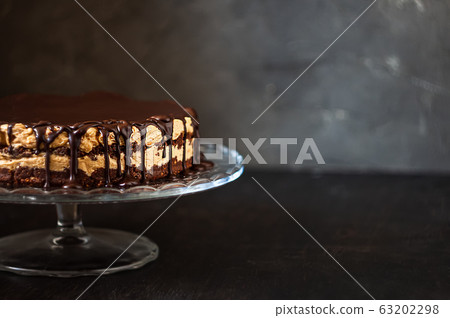 Chocolate round cake layers with butter-cream-nut cream with chocolate drips on a glass stand on a 63202298