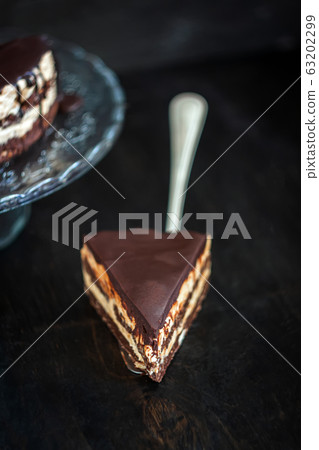 Slice and chocolate cake layers with butter-cream-nut cream with chocolate drips on a glass stand on 63202299
