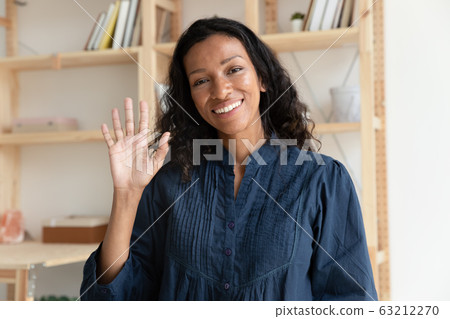 Pleasant smiling biracial woman making hello gesture, looking at camera. 63212270