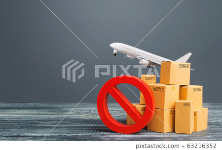 Cardboard boxes near a prohibition symbol NO and freight plane. Restrictions ban on import goods. Sanctions, trade embargo. Isolation quarantine. Manufacturers production slowdown. Flight cancellation 63216352