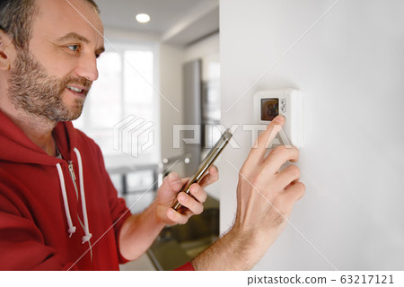 Joyful man looking at his smartphone how the temperature of the heater in a smart home is regulated 63217121