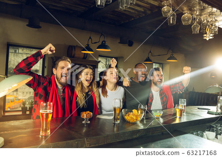Sport fans cheering at bar, pub and drinking beer while championship, competition is going 63217168
