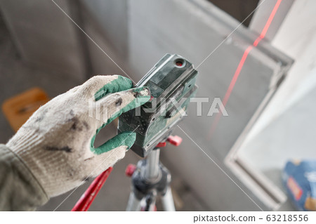 The construction worker Measures horizon level with a laser level. Construction of internal walls in the apartment using a plaster concrete plate with groove ridge. Gypsum plate The construction worker Measures horizon level with a laser level. Construction of internal walls in the apartment using a plaster concrete plate with groove ridge. Gypsum plate 63218556