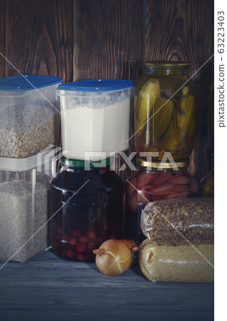 a lot of glass jars with canned food and cereals on a wooden shelf 63223403