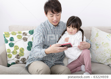 看著智能手機的父母和孩子(父親和女兒)家庭形象 看著智能手機的父母和孩子(父親和女兒)家庭形象 63224939