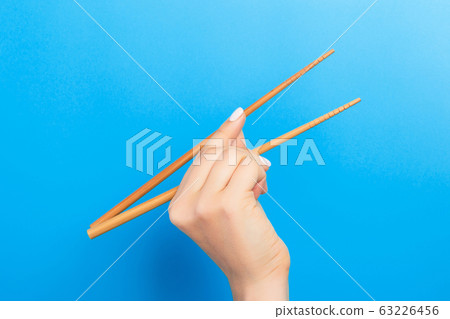 Female hand with chopsticks on blue background. Female hand with chopsticks on blue background. 63226456