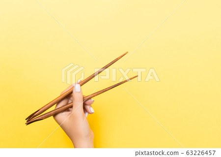 Female hand with chopsticks on yellow background. 63226457