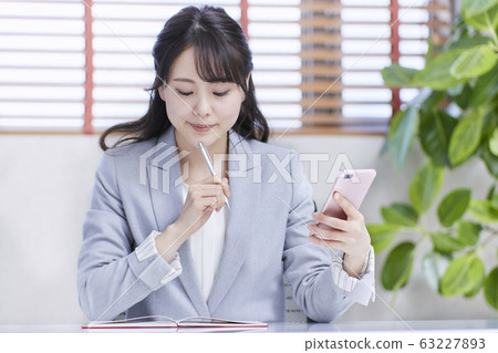 檢查日程表的年輕女商人，當看智能手機時 63227893