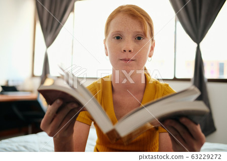 Young Redhead Girl Studying And Showing Book To Camera Young Redhead Girl Studying And Showing Book To Camera 63229272