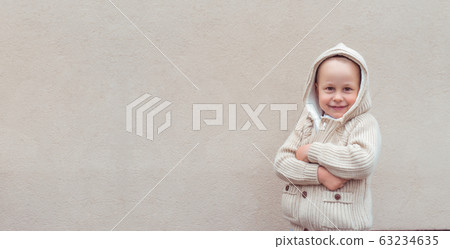 Happy joyful little boy 4-5 years old, standing in beige jumper with hood, background wall, cheerful on positive. Free space for copy text, banner for tagline. Emotions relaxation fun joy celebration. Happy joyful little boy 4-5 years old, standing in beige jumper with hood, background wall, cheerful on positive. Free space for copy text, banner for tagline. Emotions relaxation fun joy celebration. 63234635