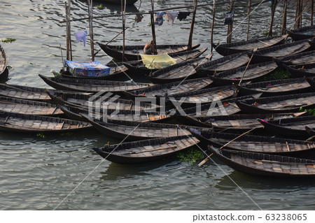 孟加拉國達卡，許多小船停在布里貢加河沿岸，一名男子和一個睡在蚊帳上的男子一起工作 63238065