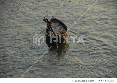 Bangladeshi man rowing a small boat on the Brigonga River in Dhaka, Bangladesh 63238088