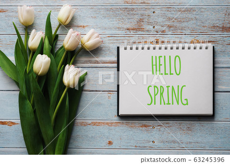 Bouquet of white flowers of tulips on the background of blue boards with a notebook with lettering Hello Spring 63245396