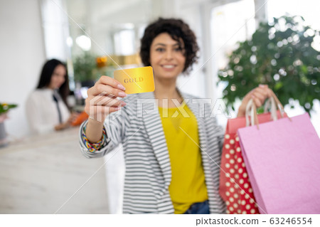 Curly-haired pretty woman holding a discount card in hands 63246554