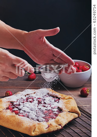 Woman's hands sprinkling fresh baked strawberry pie 63249754