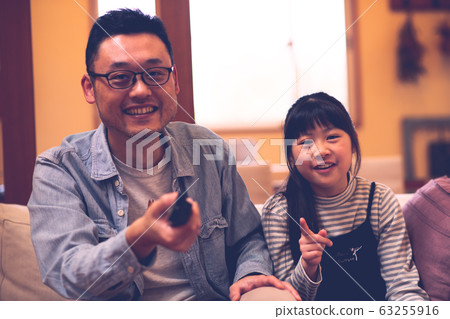 兩個父母和孩子(父親和女兒)在沙發上看電視的圖像(電影風格) 兩個父母和孩子(父親和女兒)在沙發上看電視的圖像(電影風格) 63255916