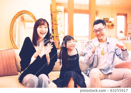 三個父母和孩子(父親,母親和女兒)在沙發上看電視的圖像(電影風格) 三個父母和孩子(父親,母親和女兒)在沙發上看電視的圖像(電影風格) 63255917