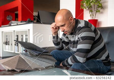 the man chooses the color of the new carpet according to the pattern book in the flooring shop 63256142