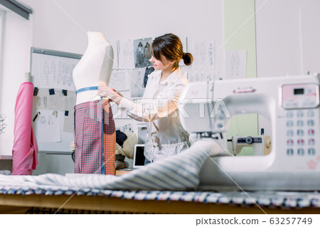 attractive brunette woman fashion designer seamstress measuring mannequin in her fashion atelier 63257749