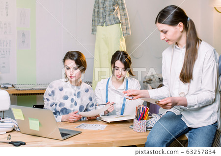 Group of three pretty women fasion designers working with clothes drawings at the table with tailoring tools and laptop 63257834