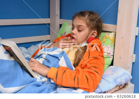Sick girl sneezes lying in bed and reading a book Sick girl sneezes lying in bed and reading a book 63260618